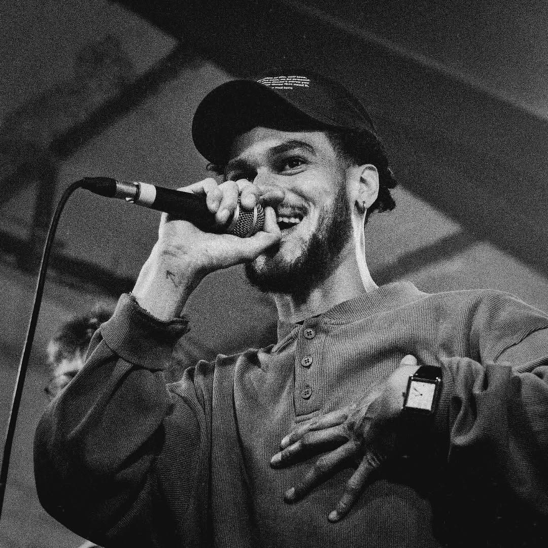 Black and white portrait of OSK in a cap, laughing into a handheld microphone.
